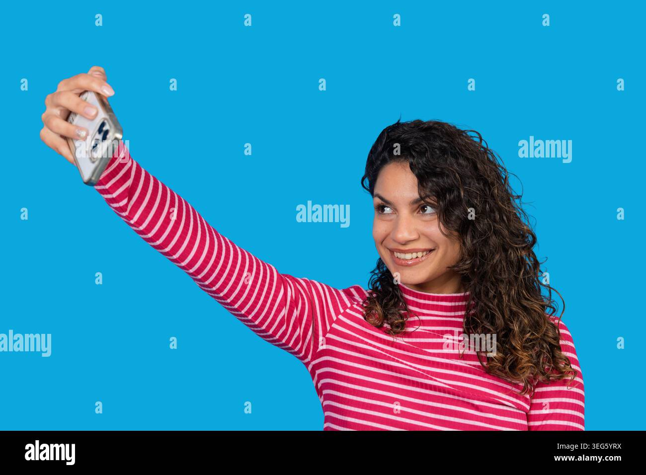 Eine junge Frau lächelt und hält ein Smartphone in der Hand, um einen Moment in den sozialen Medien festzuhalten Stockfoto