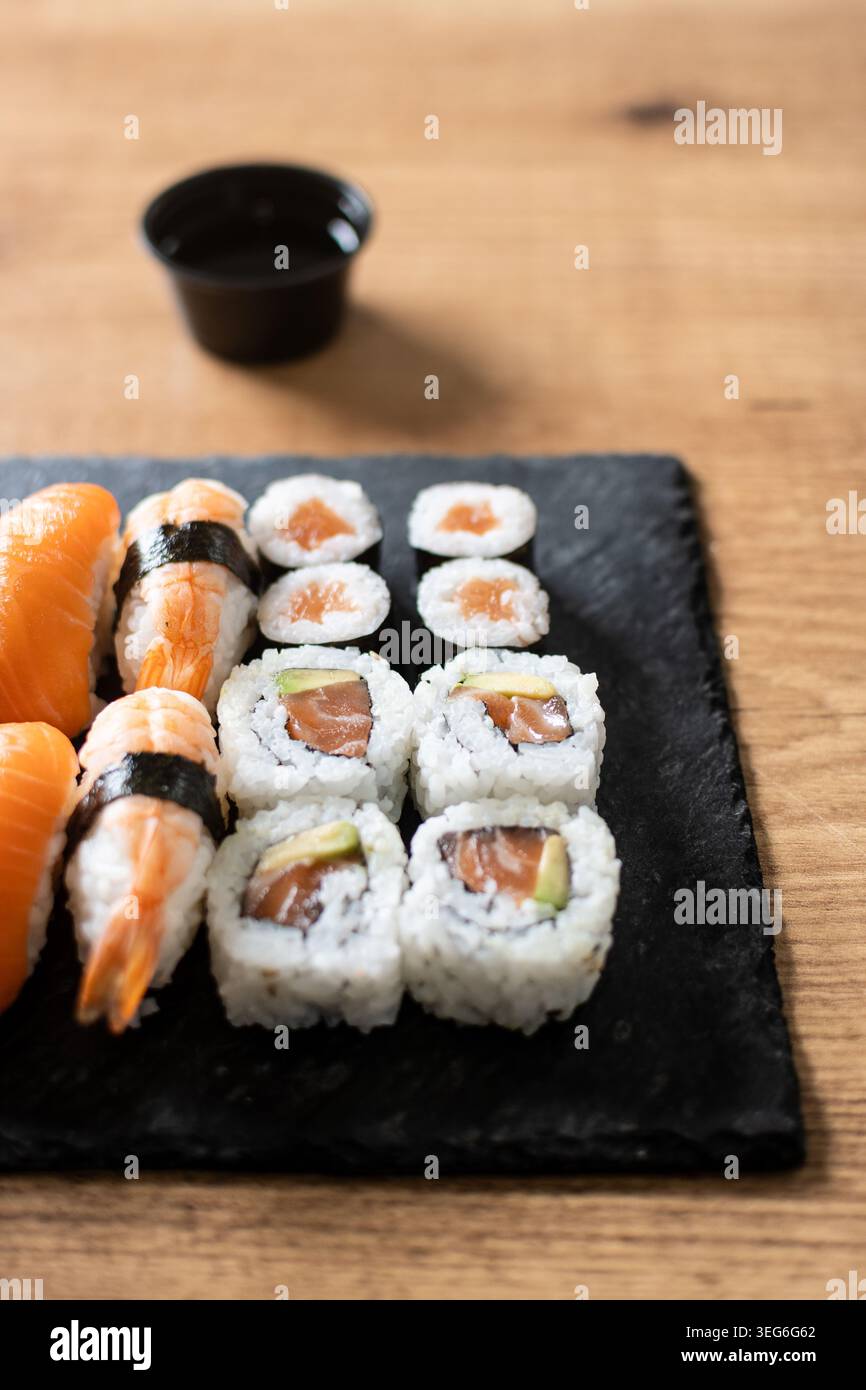 Frisches Sushi-Sortiment mit Lachs-Maki und Nigiri auf schwarzem Schieferbrett Stockfoto