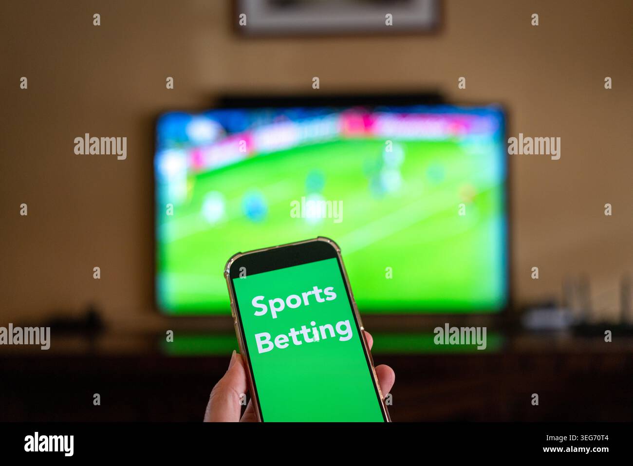 Sportwetten-Nachricht auf dem Telefon mit defokussiertem tv-Bildschirm, auf dem ein Fußballspiel im Hintergrund angezeigt wird. Stockfoto