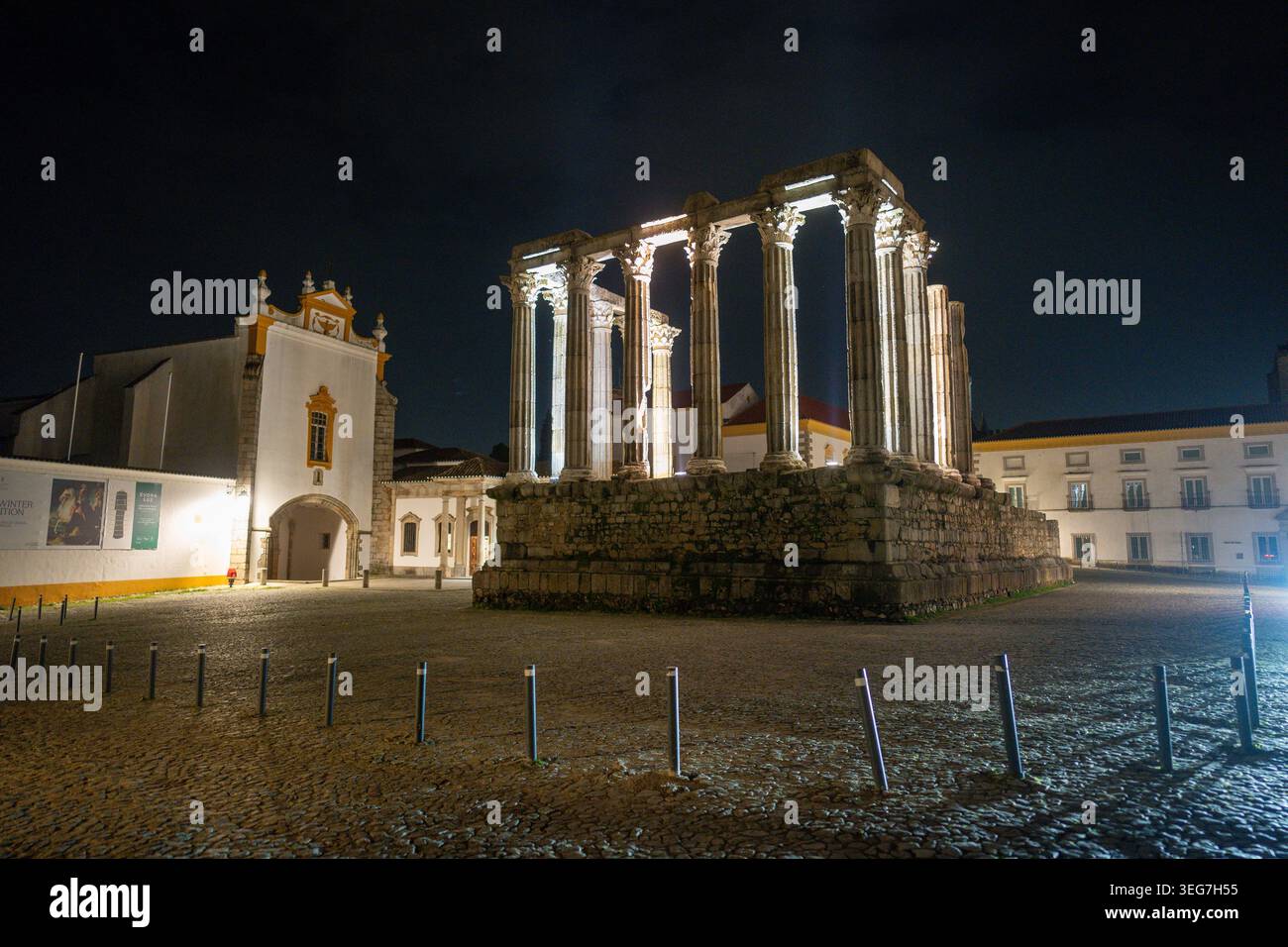 Beleuchtete römische Tempelruinen bei Nacht in Evora, Portugal, mit antiken Steinsäulen, Kopfsteinpflasterplatz und historischer Architektur mit Atmosp Stockfoto