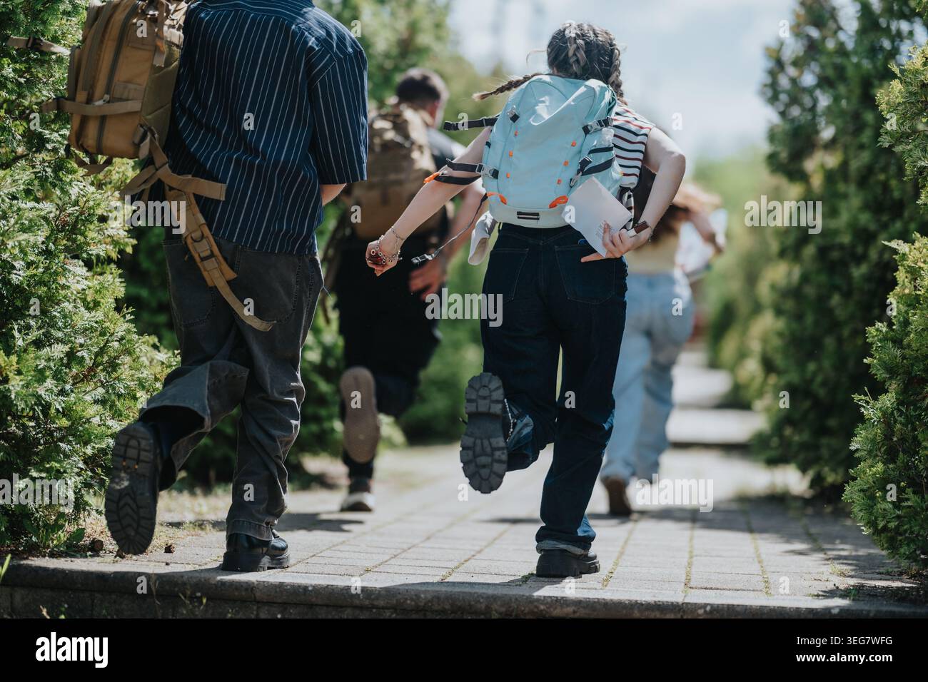 Kinder mit Rucksäcken laufen zusammen auf einem sonnigen Freiweg in Richtung Schule oder Abenteuer Stockfoto