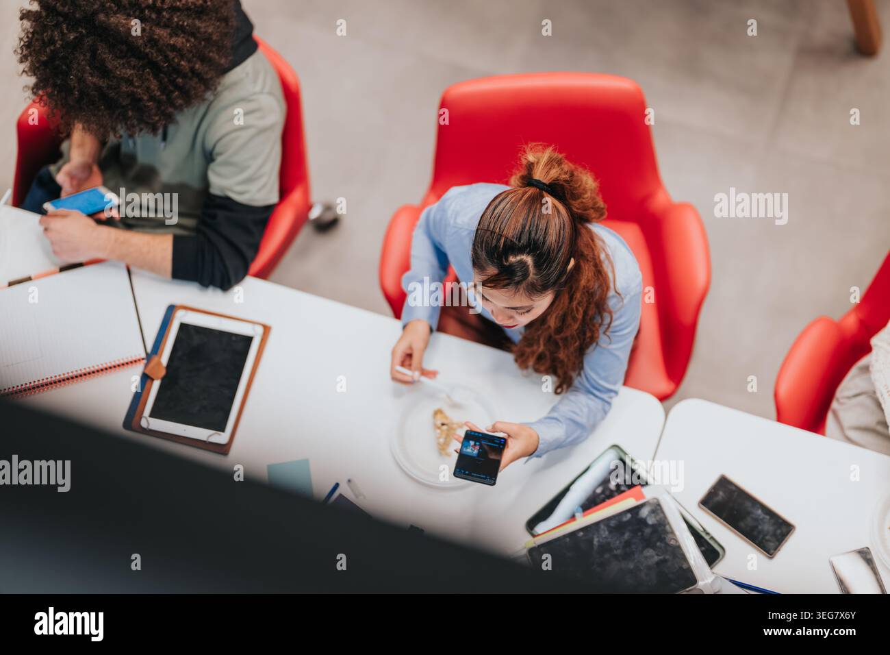 Junge Profis, die eine Pause mit Snacks und Geräten an einem ungezwungenen Arbeitsplatz machen Stockfoto
