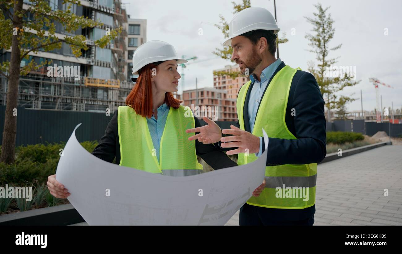 Kaukasier zwei Kollegen Baumeister Architekten Frau Mann diskutieren Blueprint Plan Kollegen Ingenieure Frau männlich in Helmen Hardhelme Westen Papier Dokument Stockfoto