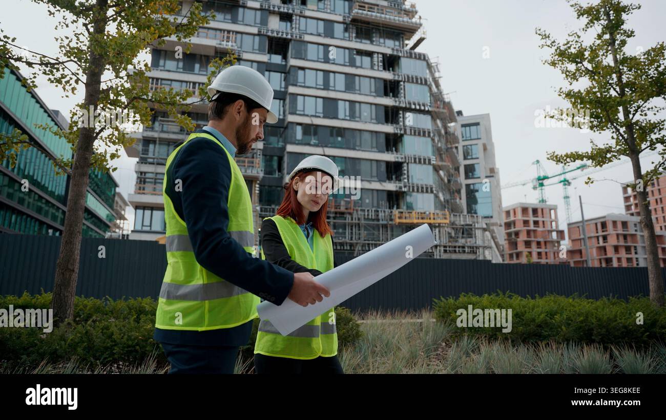Zwei Architekten bauen Arbeiter Kaukasische Frau Mann Ingenieure diskutieren Plan Bau weibliche männliche Kollegen Partner in Sicherheitshut reflektierende Weste reden Stockfoto