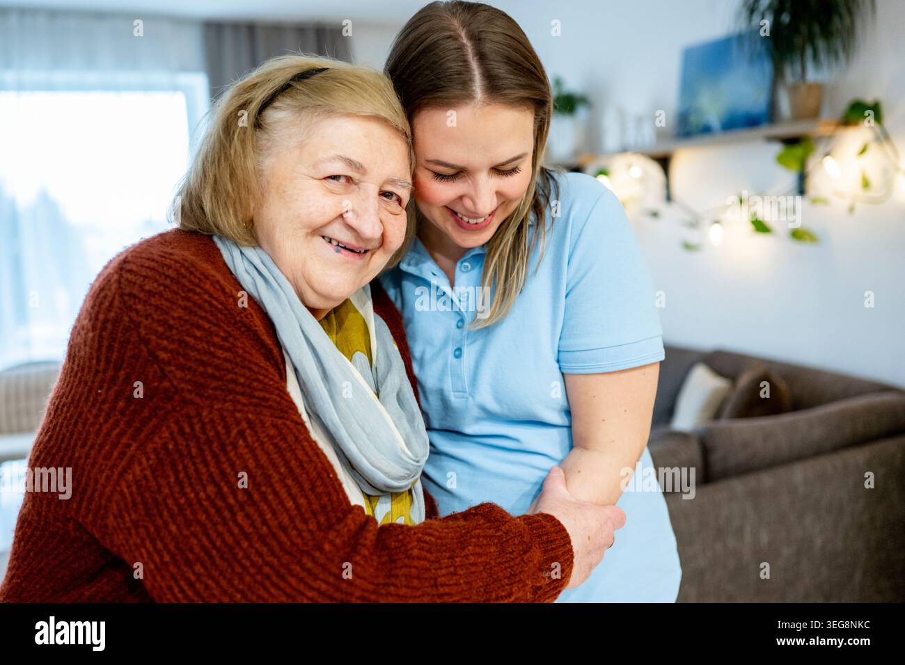 Fürsorgliche Pflegekraft, die glückliche Seniorin zu Hause umschließt. Stockfoto