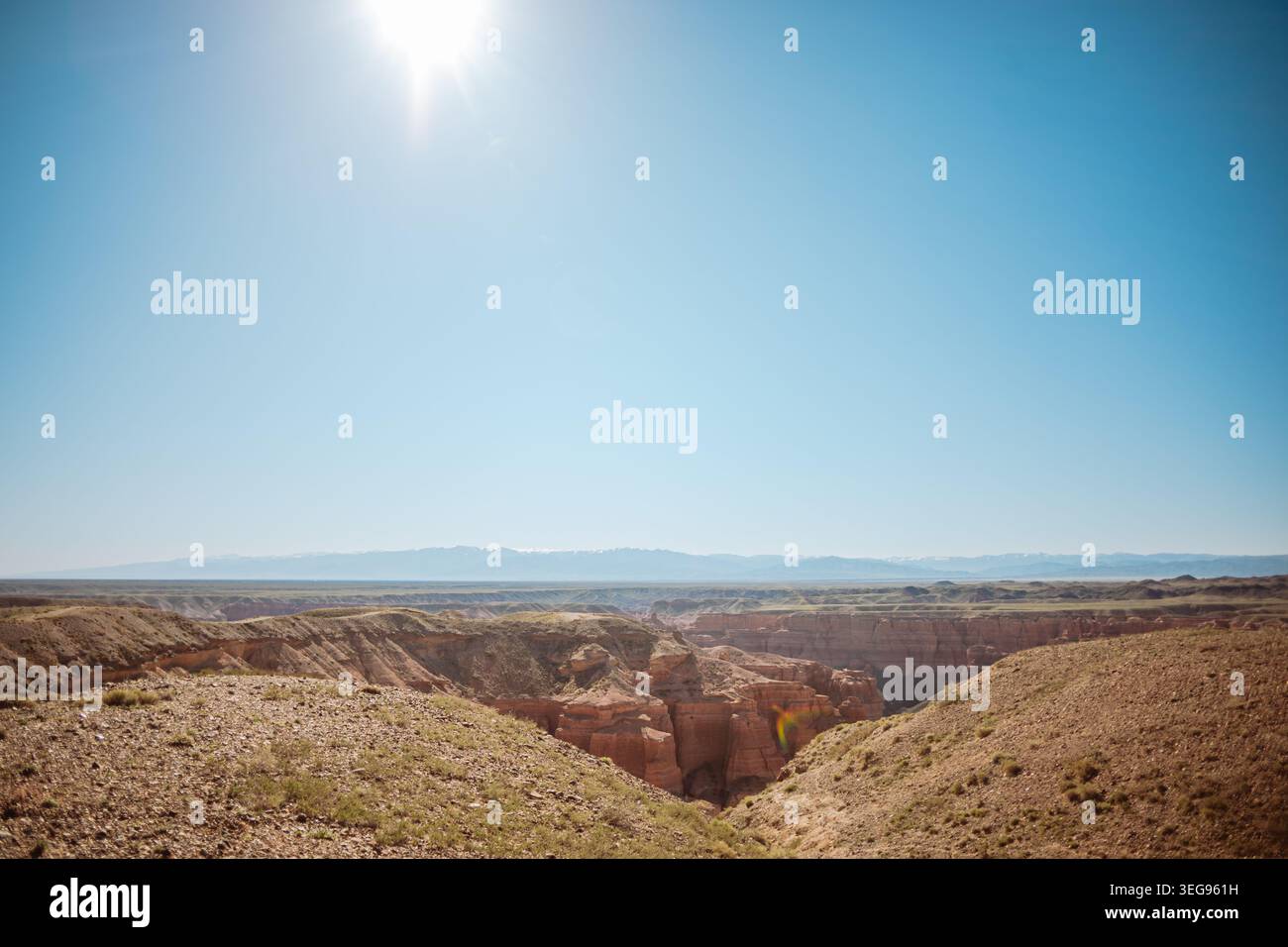 Panoramablick auf einen tiefen, dramatischen Canyon mit rötlichen Felsformationen, erodierten Klippen und sanften trockenen Hügeln unter intensivem hellem Sonnenlicht und klarem bl Stockfoto