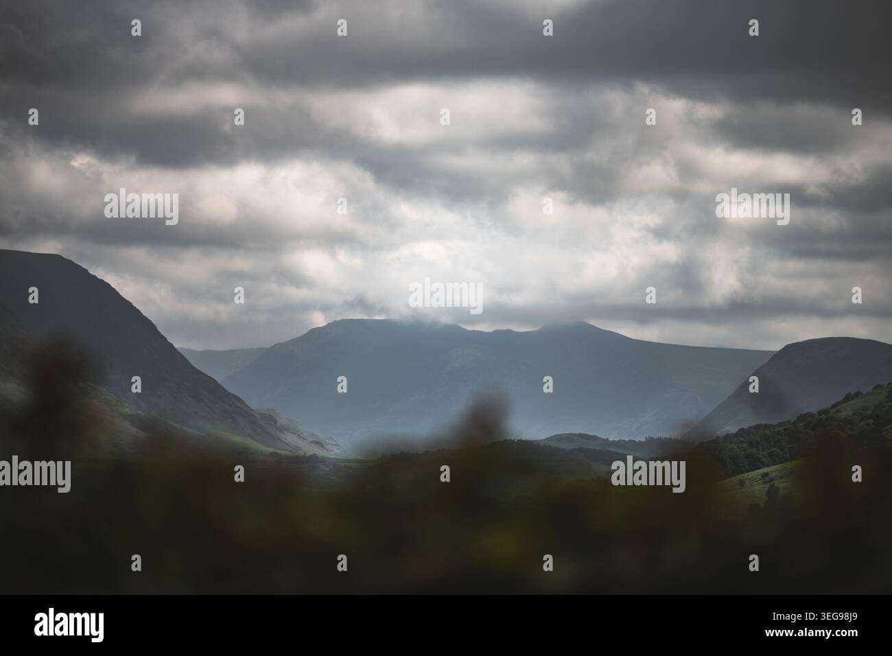 Die stimmungsvolle Atmosphäre der Berge wird durch die dramatischen Wolken und das weiche, gestreute Licht verstärkt, das ein Gefühl von Tiefe und Größe schafft Stockfoto