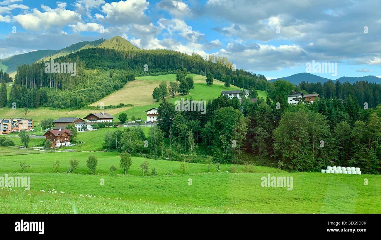Friedliche alpine Landschaft mit grünen Hügeln, Wäldern und ländlichen Häusern unter einem dramatischen Himmel - Smartphone-aufgenommenes Stockfoto