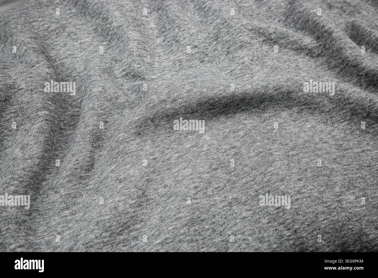 Zerknittertes graues meliertes Jersey-Material mit weichen Wellen und Schatten. Stockfoto