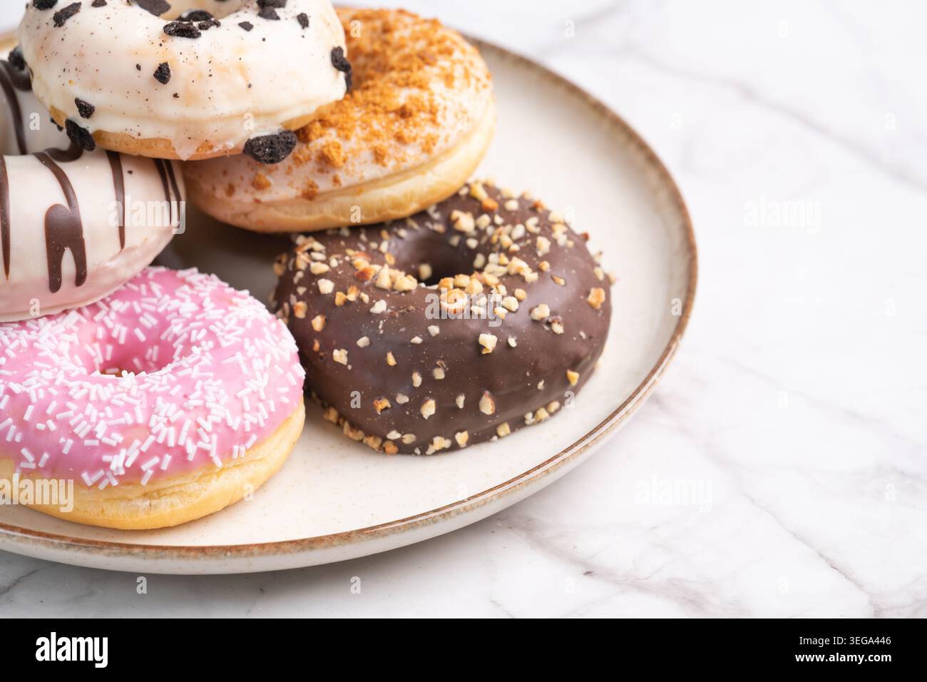 Sammlung von bunten glasierten Donuts mit verschiedenen Belägen serviert auf einer Keramikplatte über einer Marmoroberfläche. Gourmet-Bäckerei Dessertkonzept mit Kopie Stockfoto