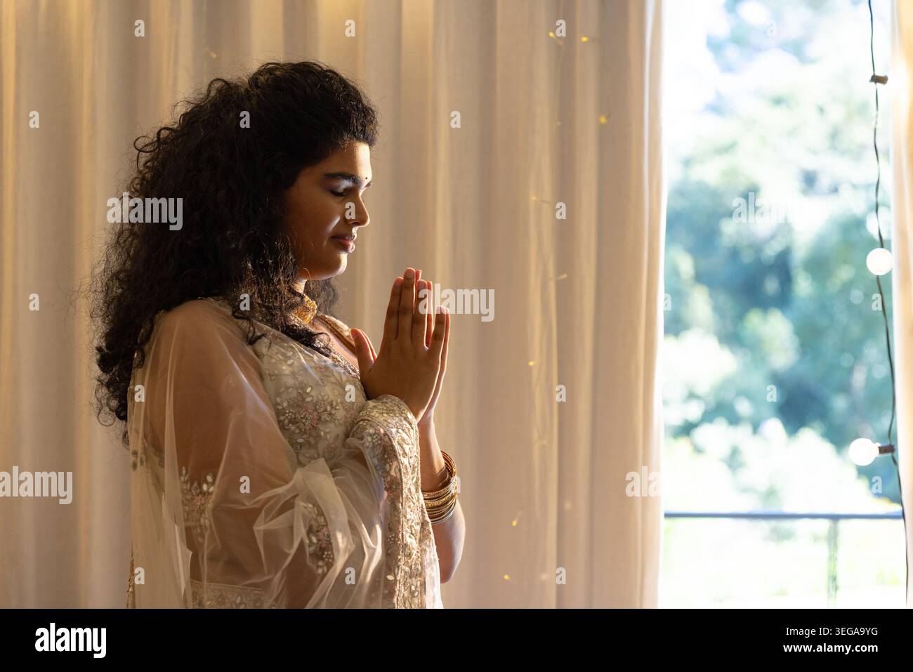 Indianerin drückt Palmen, steht am Fenster, trägt transparente Dupatta und goldene Armreifen, Kopierraum Stockfoto