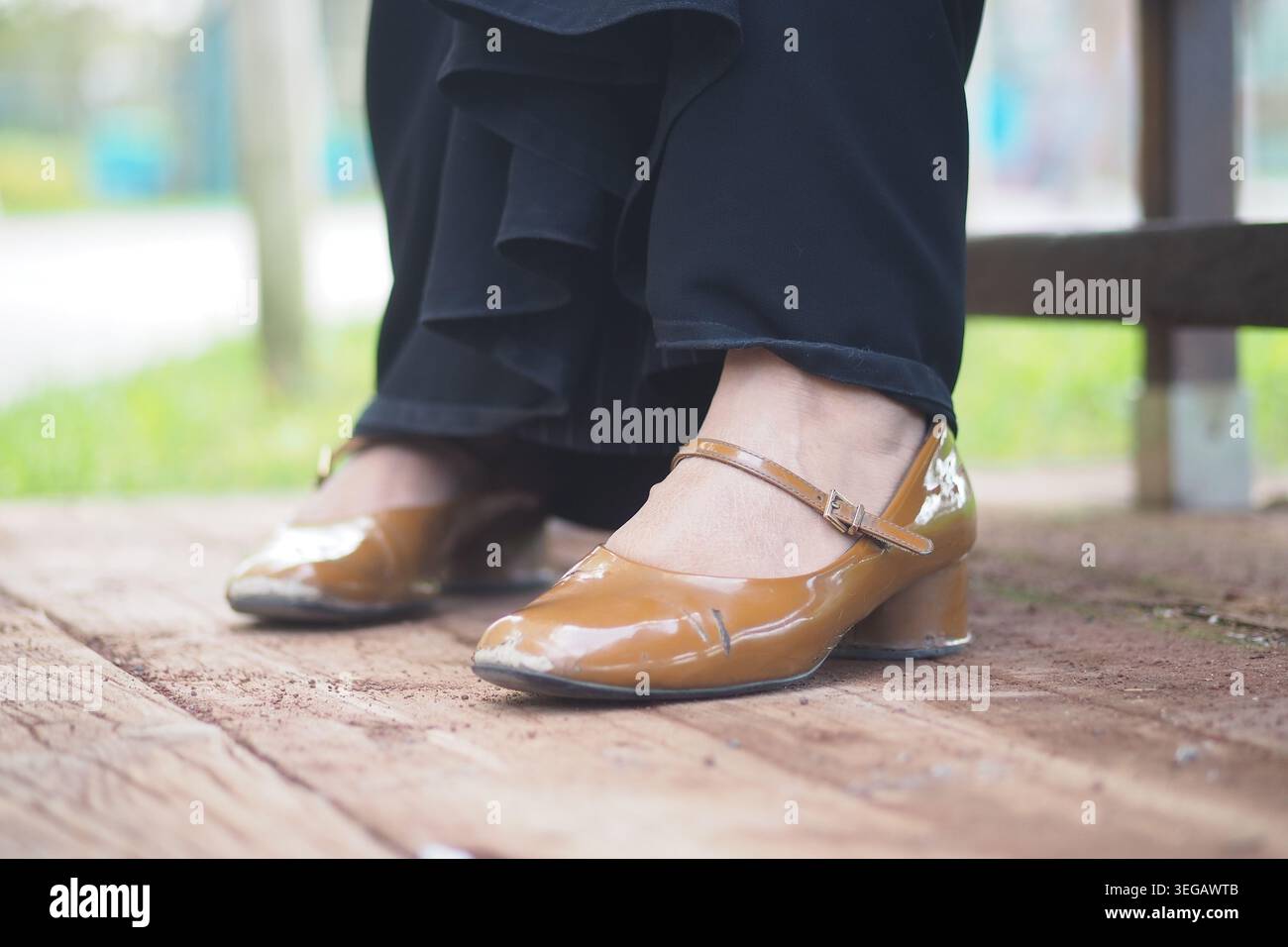Frau mit braunen Schuhen sitzt draußen auf einer Holzbank Stockfoto