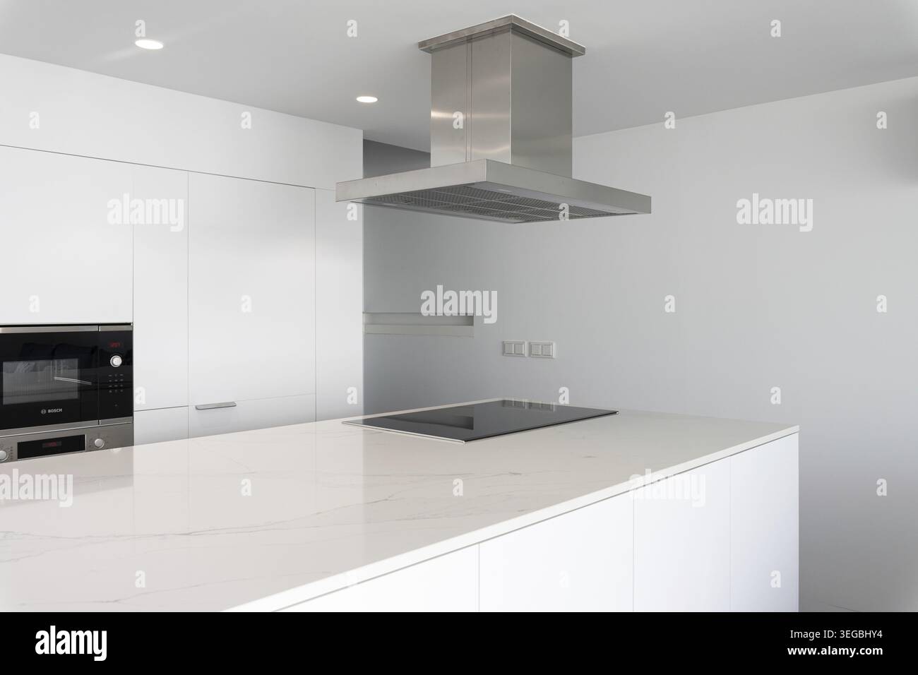 Moderne, minimalistische weiße Küche mit Insel, Kochfeld und Dunstabzugshaube Stockfoto