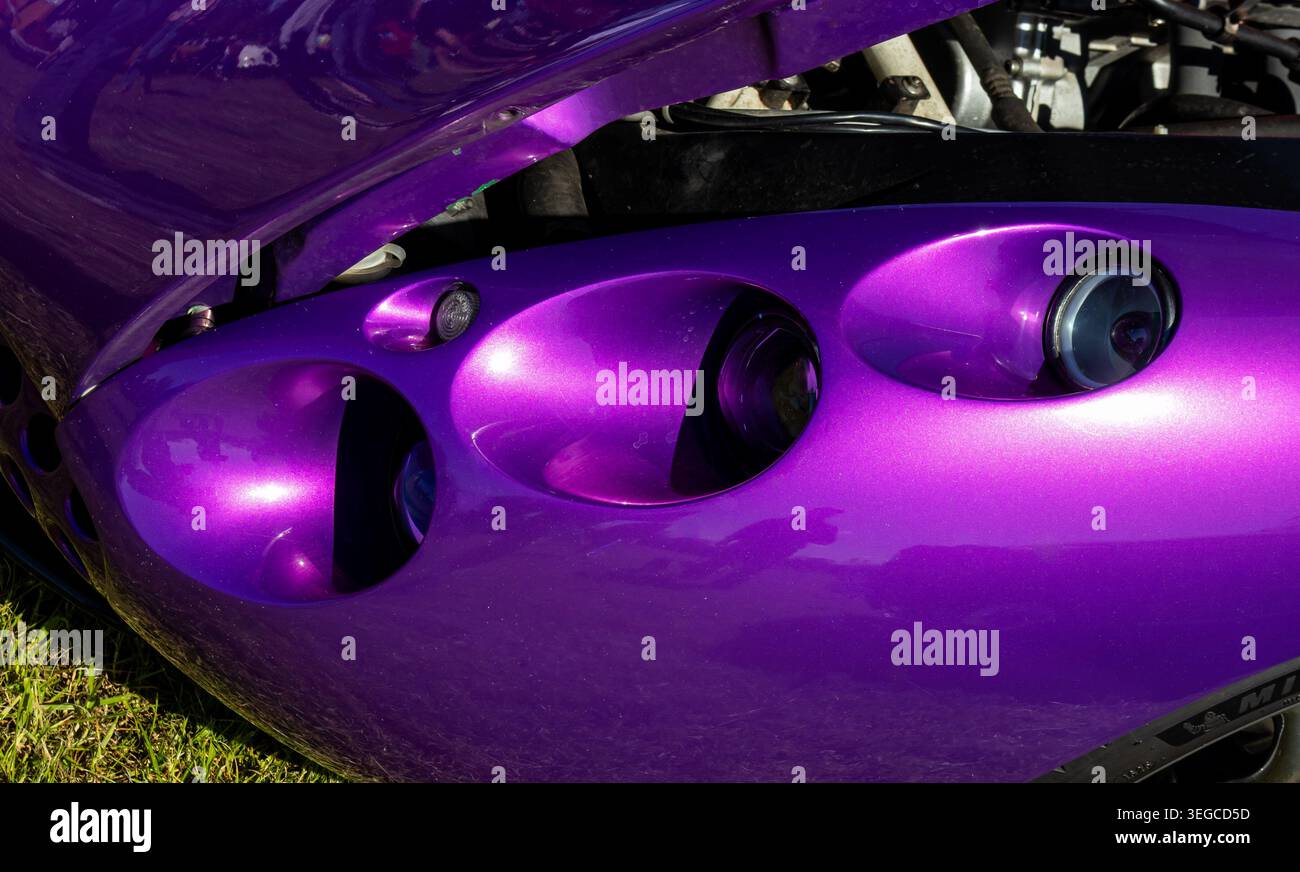 Sportwagenfront in violettem Metallic mit ovalen Scheinwerferkissen und leuchtender Bonbonfarbe, die im Sonnenlicht glänzt Stockfoto