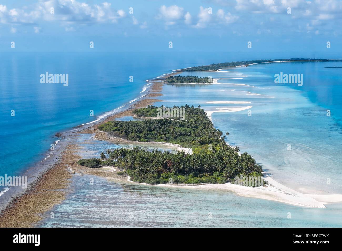 Blick aus der Vogelperspektive auf üppige tropische Inseln mit grünen Palmen und türkisfarbenen Korallenriffen, umgeben vom tiefblauen Ozean unter einem klaren Himmel in der Nähe von Vaanee, Stockfoto