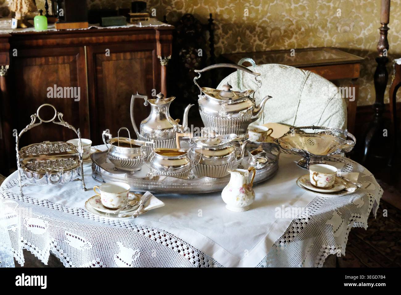Verziertes viktorianisches Teeservice und feine porzellanteetassen auf einer weißen Tischdecke in einem prächtigen Speisesaal. Stockfoto
