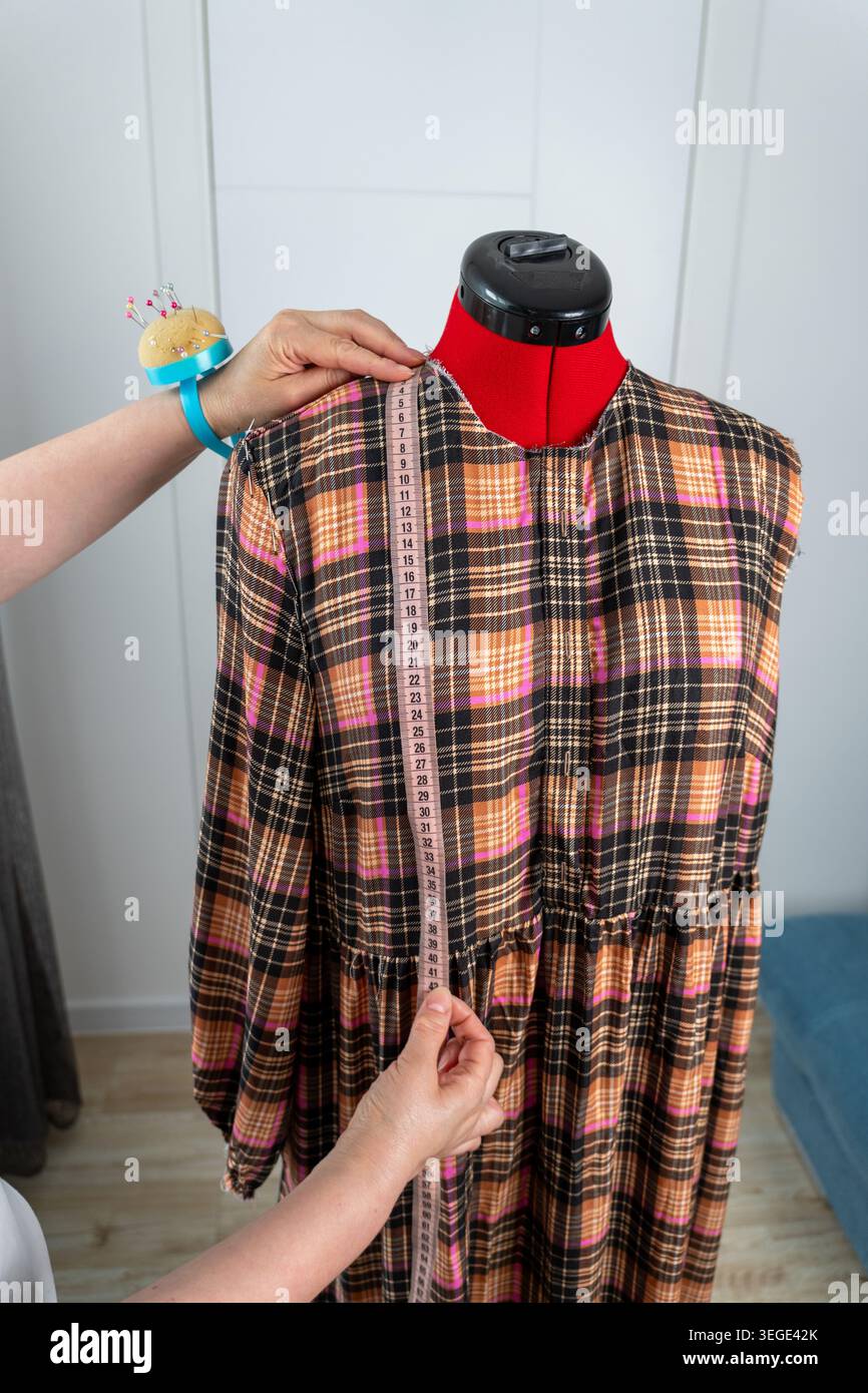 Vertikalansicht einer Frau, die während der Schneiderei und des Nähprozesses im Atelier Messungen an einer professionellen Schneiderpuppe durchführt. Modedesigner arbeitet Stockfoto