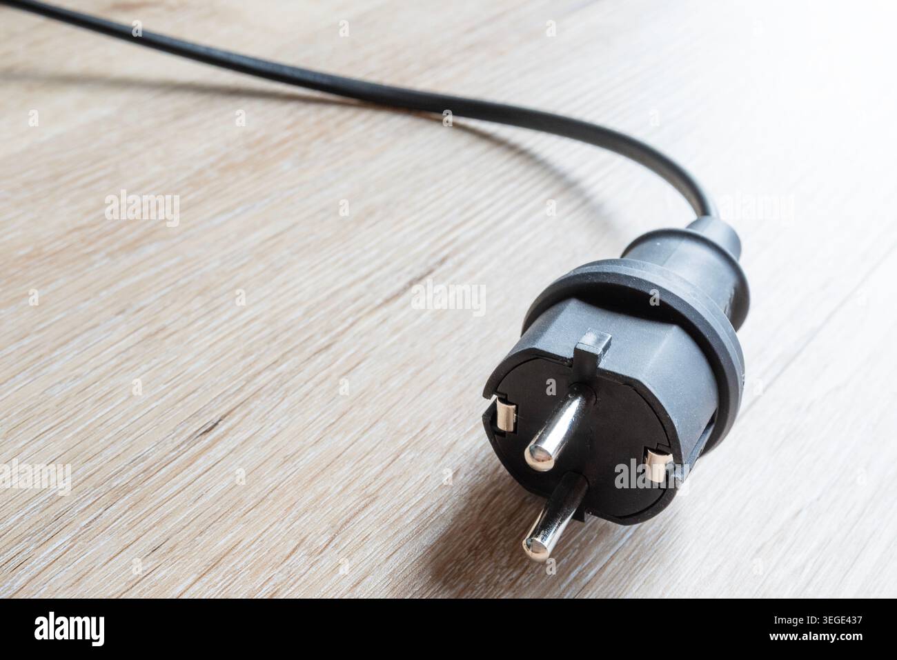 Nahaufnahme des schwarzen Schuko-Sicherheitssteckers mit Kabel auf hellem Holzboden Stockfoto