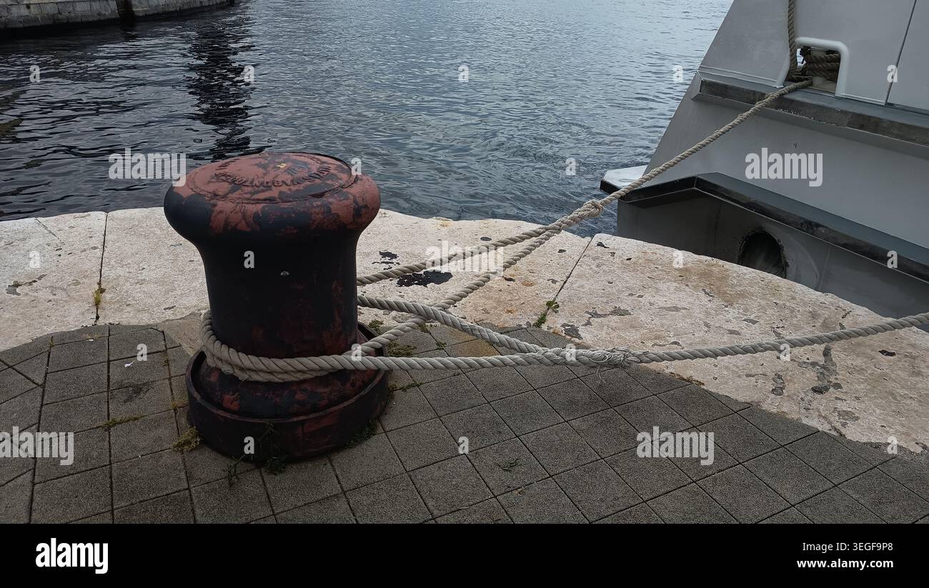 Nahaufnahme eines rostigen eisernen Schiffspollers mit einem Hochleistungs-Seeseil, das an einem Pier um ihn gebunden ist. Stockfoto