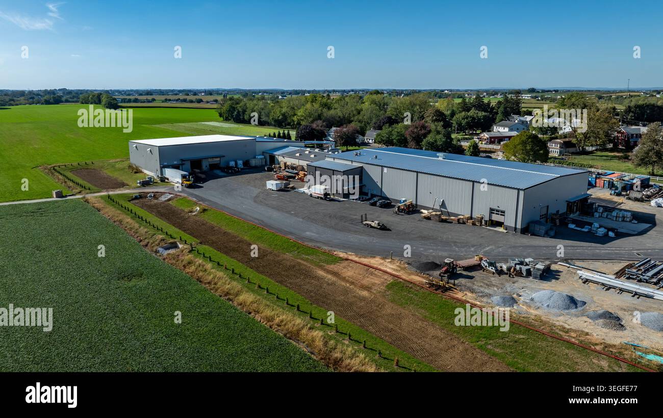 Große Bauernhäuser sind in ländlicher Umgebung zu sehen. Grüne Felder umgeben das Gebiet, und Ausrüstung befindet sich in der Nähe. Der Himmel ist klar und hell. Stockfoto