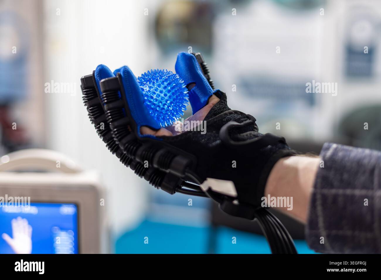 Roboterhandschuh hält Therapieball. Nahaufnahme eines robotischen Rehabilitationshandschuhs, der einen blauen Therapiekugel für Handerholung und Grip hält Stockfoto