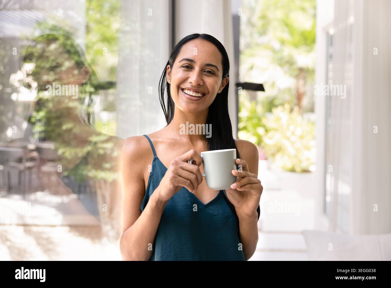 Lächelnde Frau trinkt Kaffee in der Nähe des Fensters zu Hause Stockfoto
