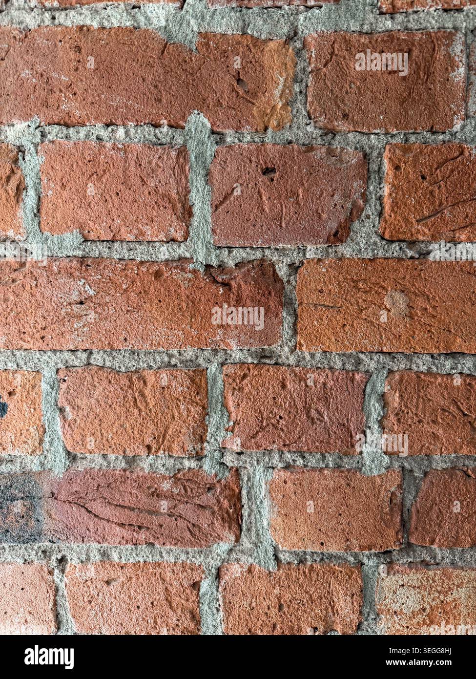 Strukturierte rote Ziegelwand mit sichtbaren Mörtelfugen und unregelmäßigen Oberflächenmustern, die eine rustikale und industrielle Ästhetik vermitteln Stockfoto