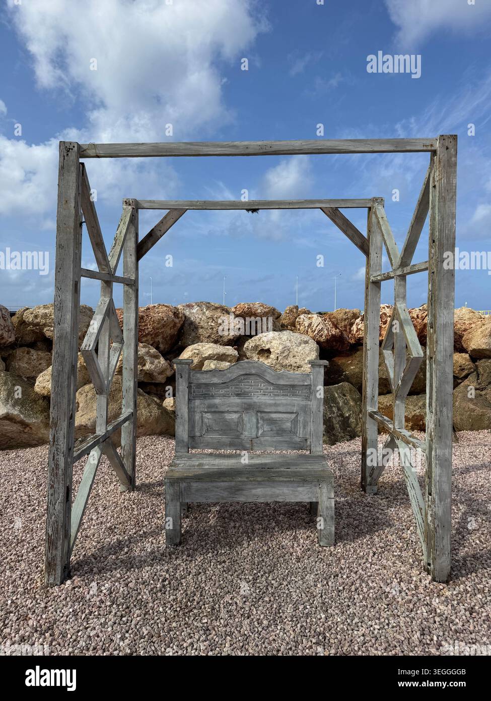 Eine rustikale hölzerne Schaukelbank an einem Kiesstrand mit Blick auf das Meer in Curacao. - Smartphone-aufgenommenes Stockfoto