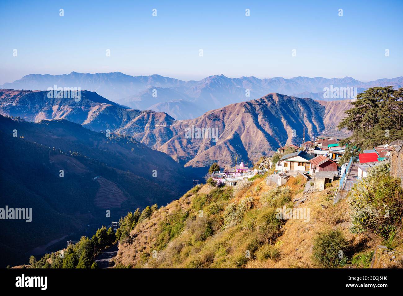 Ein malerischer Blick auf eine abgelegene Bergsiedlung auf einem steilen Hügel mit mehrschichtigen Berggipfeln im Hintergrund in Chakrata, Uttarakhand, Indi Stockfoto