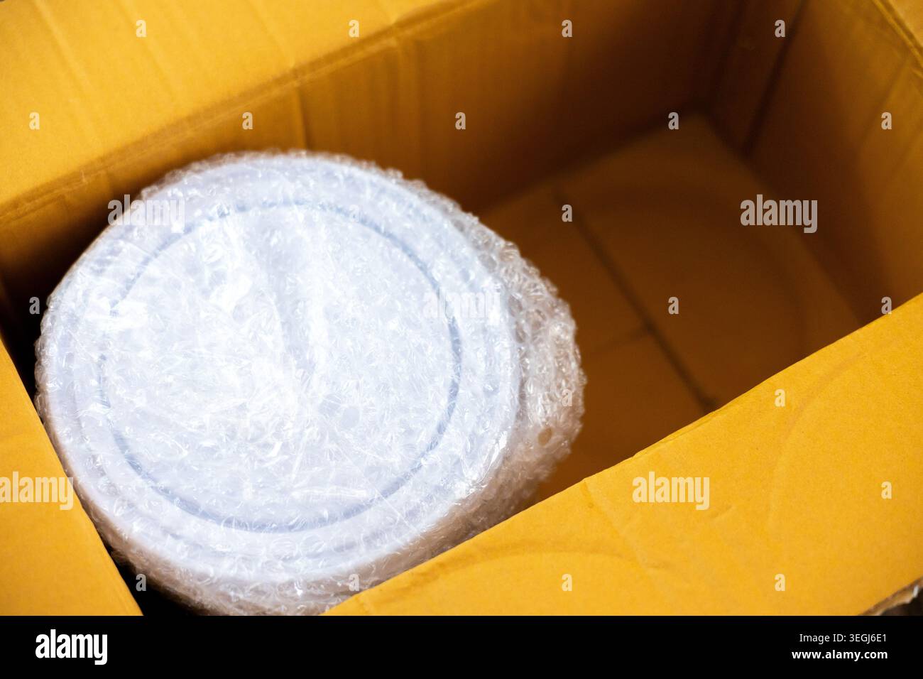 Nahaufnahme des runden Objekts, das sicher in einer schützenden Luftpolsterfolie verpackt ist und in einem großen braunen Versandkarton aus Karton für den sicheren Transport bereit ist Stockfoto