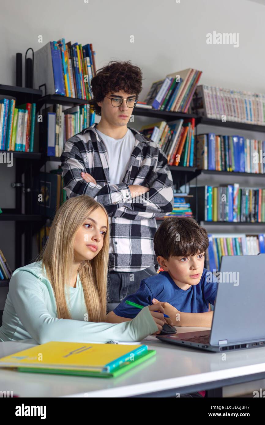 Kinder, die mit einem Laptop in der Bibliothek lernen, während ältere Schüler betreuen und helfen. Bildung, Nachhilfe, Teamarbeit, digitales Lernen und akademische Unterstützung Stockfoto