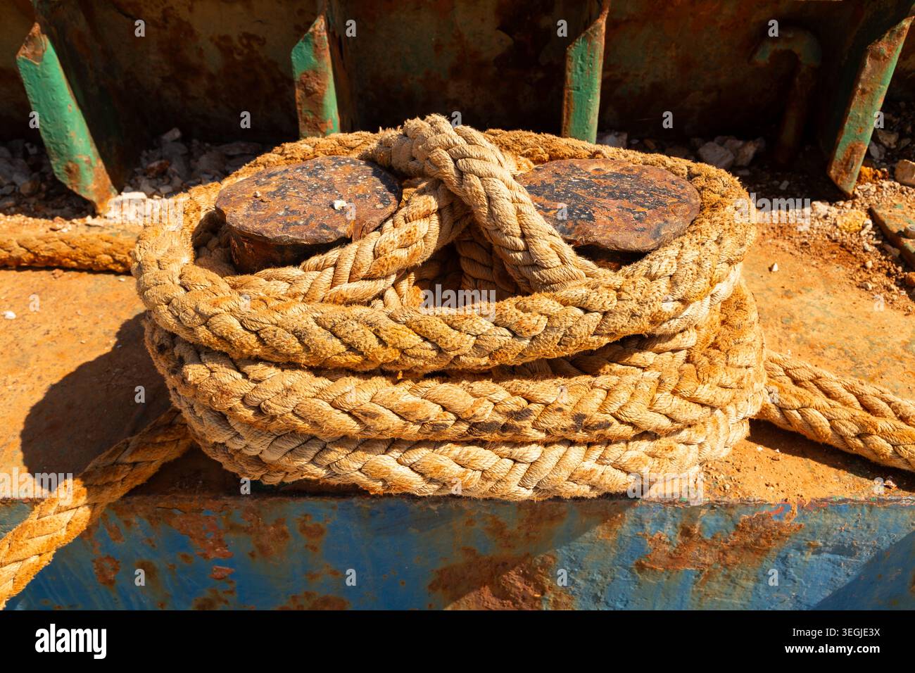 Nahaufnahme eines gewickelten Anlegeseils, das um rostige Metallpfoller an einem kleinen Pier im Hafen von Rovinj, Kroatien, gebunden ist. Stockfoto