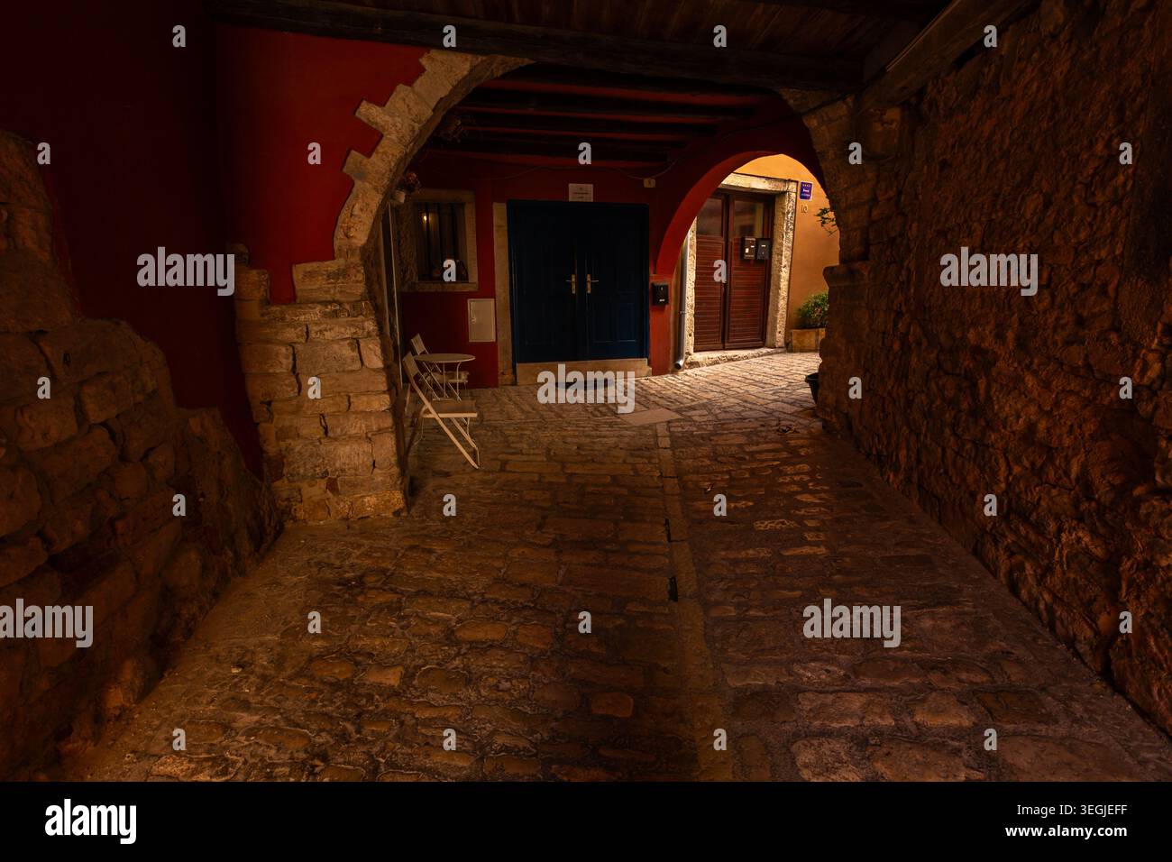 Korridor mit Steinbögen mit weißen Stühlen und dunkelblauer Tür in der Altstadt von Rovinj, Kroatien. Stockfoto