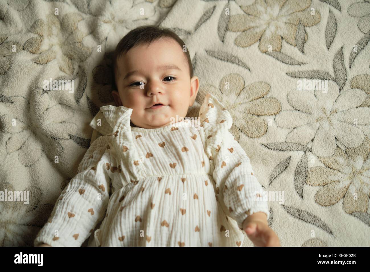 Die Zufriedenheit des Babys liegt auf einem weichen, gemusterten Hintergrund. Es ist ein universeller Moment, der die Freuden des neuen Lebens berührt. Stockfoto