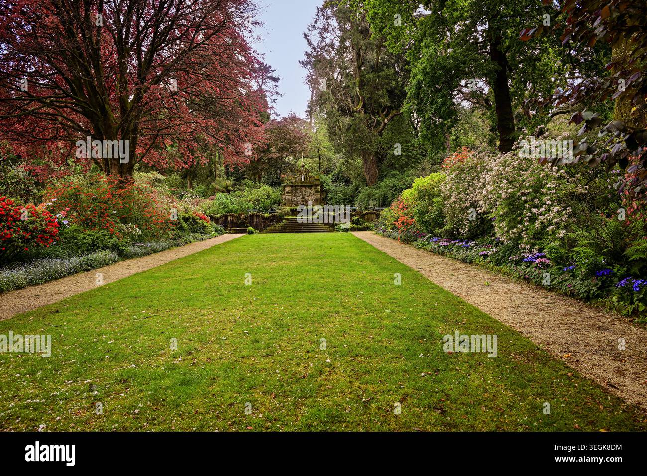 Ein wunderschön gepflegter formeller Garten gesäumt von bunten blühenden Bäumen, gepflegten Rasenflächen und üppigem Grün. Stockfoto