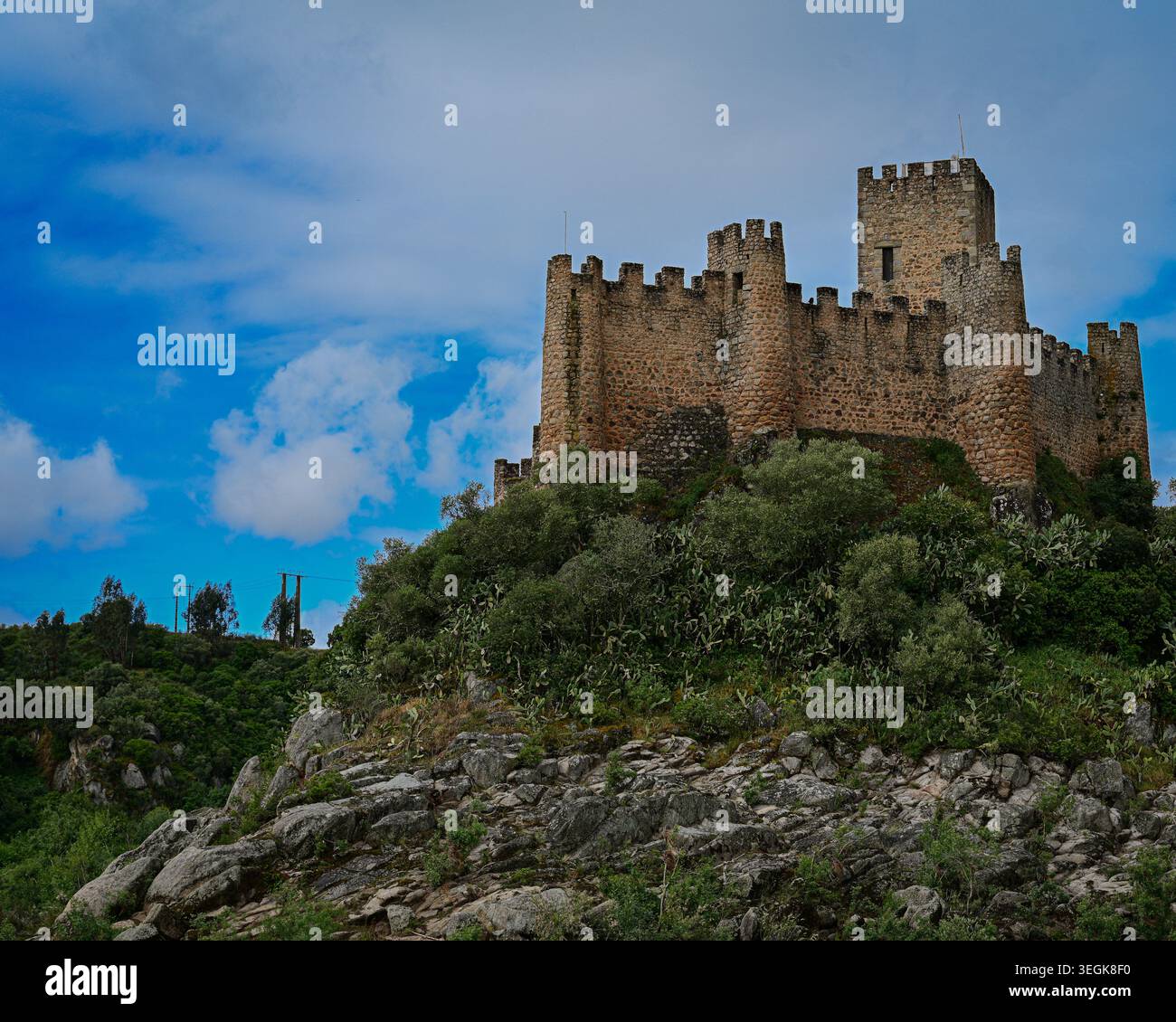Eine eindrucksvolle mittelalterliche Steinburg, die auf einem zerklüfteten Hügel unter dramatischem blauen Himmel und hohen Wolken thront. Stockfoto