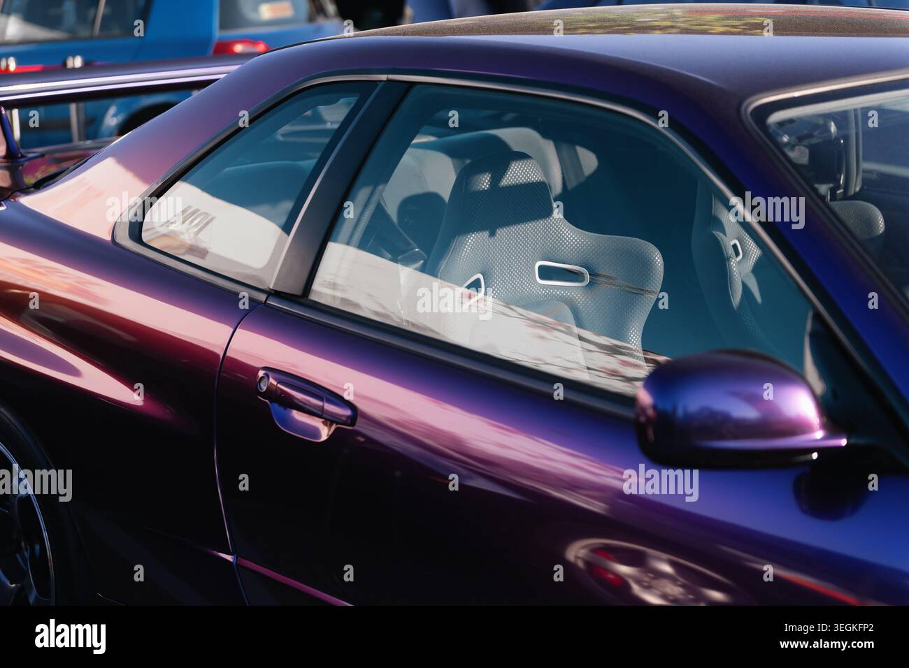 Nahaufnahme des lilafarbenen Nissan Skyline R34 GT-R Coupés auf dem Parkplatz, der den Sportschalensitz bei hellem Sonnenlicht hervorhebt. Stockfoto