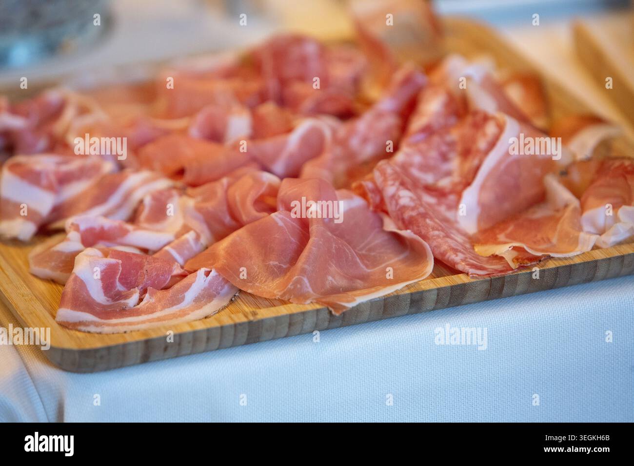 Verschiedene aufgeschnittene Wurstwaren einschließlich Schinken, Pancetta und Salami auf einem Holzbrett Stockfoto