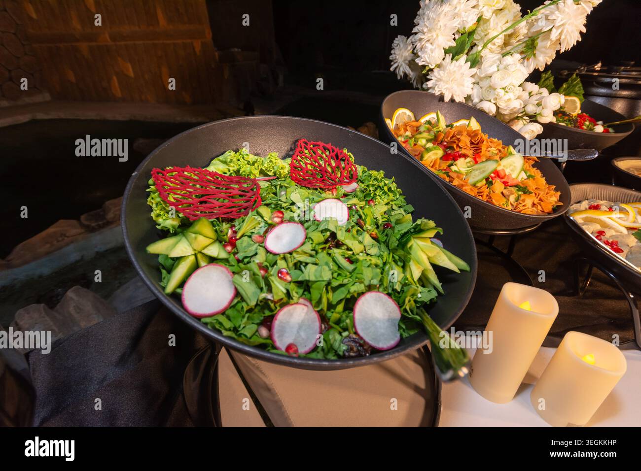 Ein Buffet mit Salaten aus dem Nahen Osten in schwarzen Schüsseln, garniert mit Radieschen, Granatapfel und essbarem Dekor Stockfoto