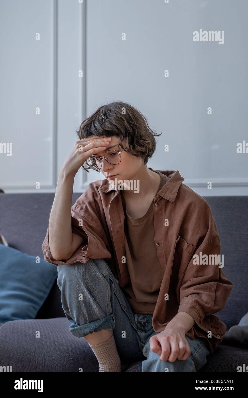 Frustriertes Teenager-Mädchen sitzt auf dem Sofa mit sorgsam nachdenklichem Ausdruck, berührt die Stirn und fühlt emotionalen Stress und mentale Erschöpfung. Angstzustände, Stockfoto