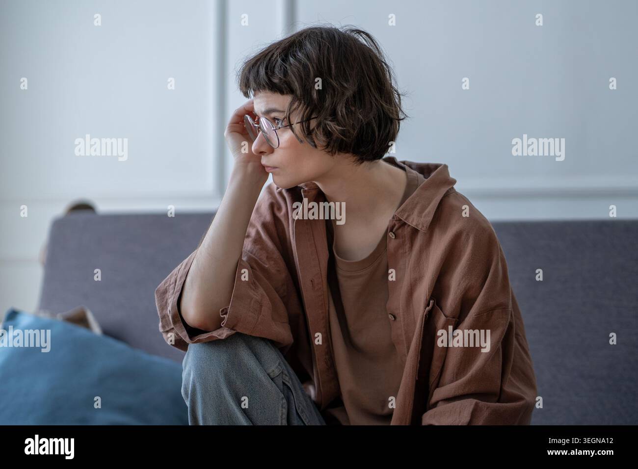 Traurige, nachdenkliche Frau, die auf dem Sofa sitzt und schweigend während eines schwierigen emotionalen Schocks wegschaut. Angst, Einsamkeit, Unsicherheit. Frustrierte junge fema Stockfoto