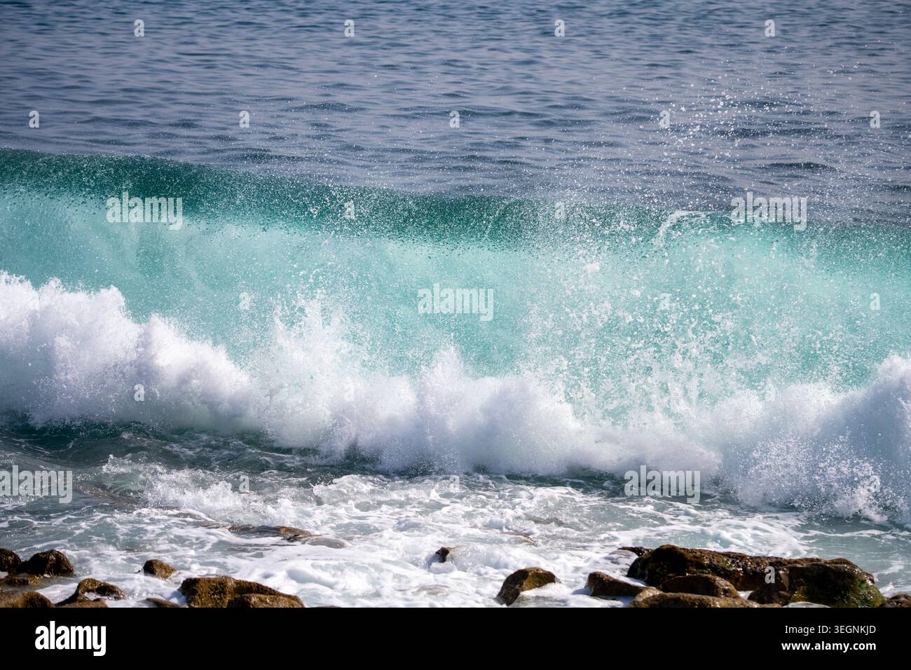 Wellen brechen an einem stürmischen Tag an einem Ufer gegen Felsen. Wasser sprüht in die Luft, während mächtige Wellen aus dem Ozean hereinströmen und eine dynamische Szene an der Küste erzeugen. Stockfoto