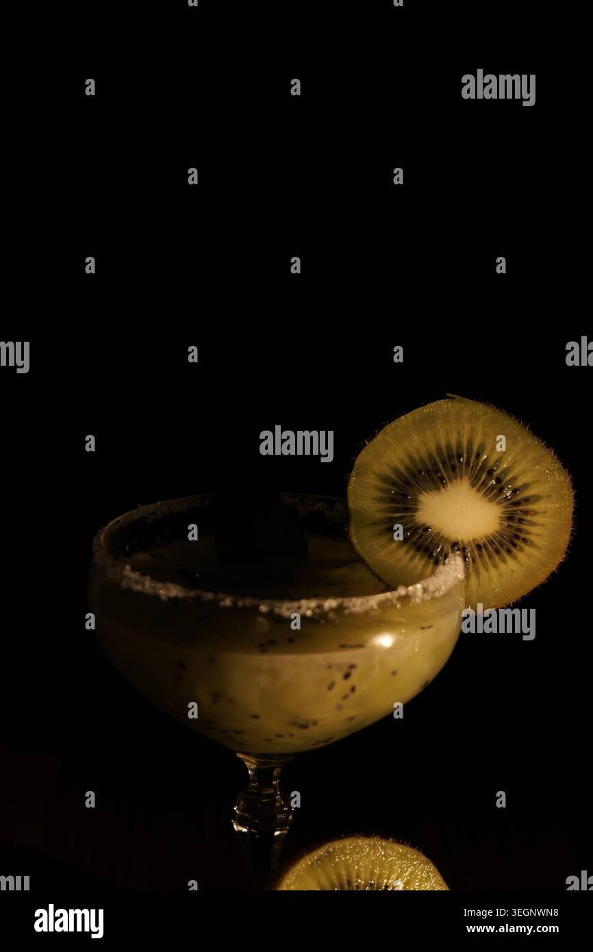 Kiwi-Cocktail mit gesalzenem Rand und frischer Kiwi-Scheibe auf dunklem Hintergrund. Das Studio in Nahaufnahme betont lebendiges Grün, elegantes Design und Refre Stockfoto