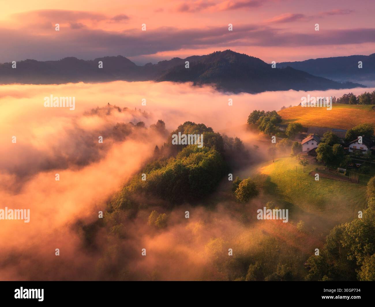 Aus der Vogelperspektive auf Wiesen und Berge in niedrigen Wolken bei Sonnenaufgang Stockfoto