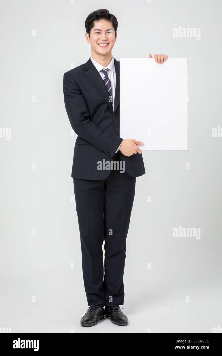 Ein junger asiatischer Profi im Business-Anzug hält ein weißes Schild. Stockfoto
