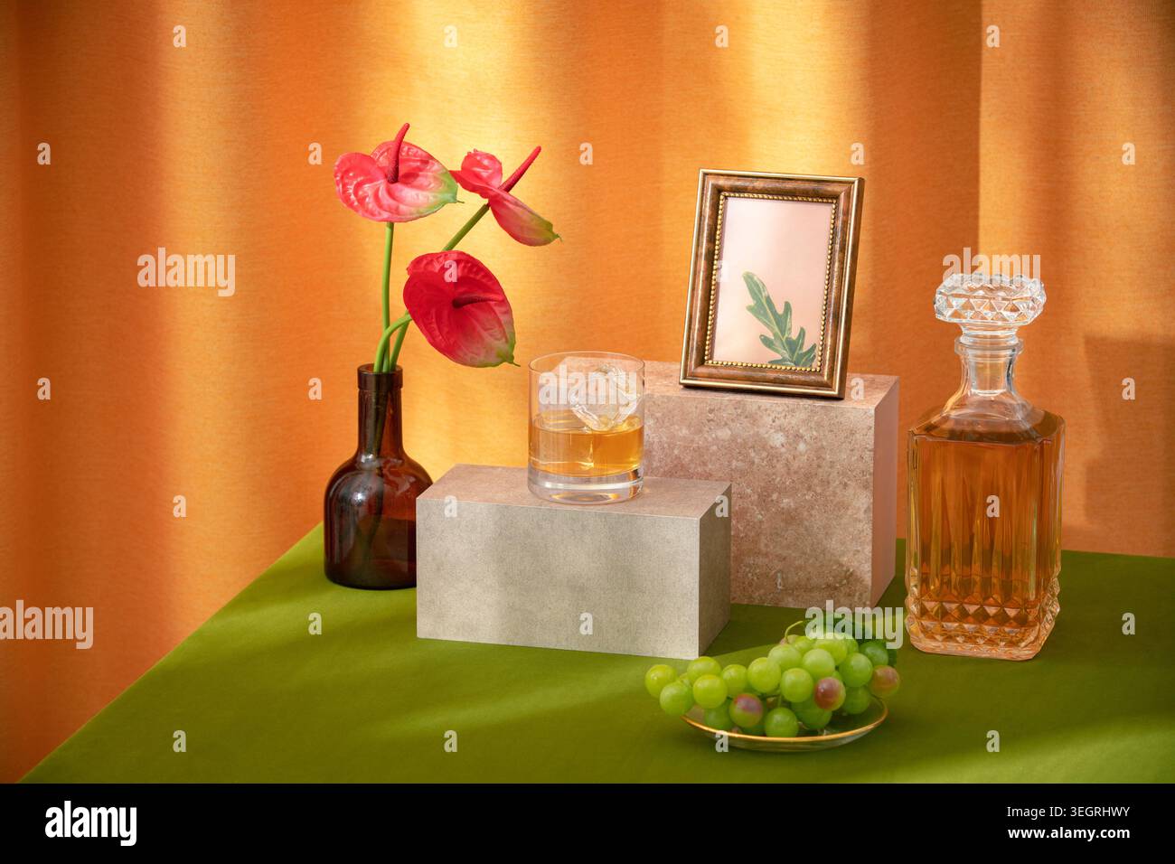 Ein Glas Whiskey sitzt auf einem Steinsockel inmitten eines Stilllebens aus Blumen, Früchten und gerahmtem botanischem Druck. Stockfoto