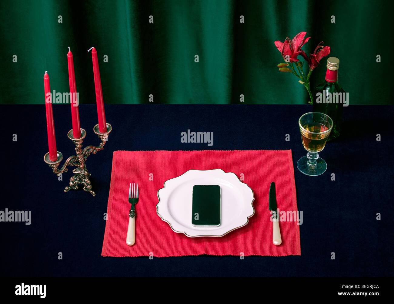 Ein Smartphone wird auf einem Teller platziert, umgeben von Kerzen, Blumen und einer Flasche Wein, in einer ruhigen, intimen Abendumgebung. Stockfoto