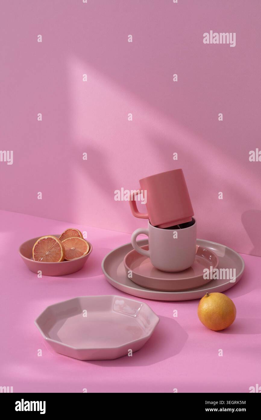 Ein Stapel rosafarbene und weiße Keramik und eine Schüssel Zitrusscheiben auf einer rosa Tischdecke. Stockfoto