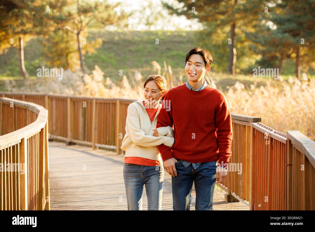 Ein junges Paar geht Hand in Hand durch einen sonnigen Wald, lacht und genießt die Gesellschaft des anderen. Stockfoto
