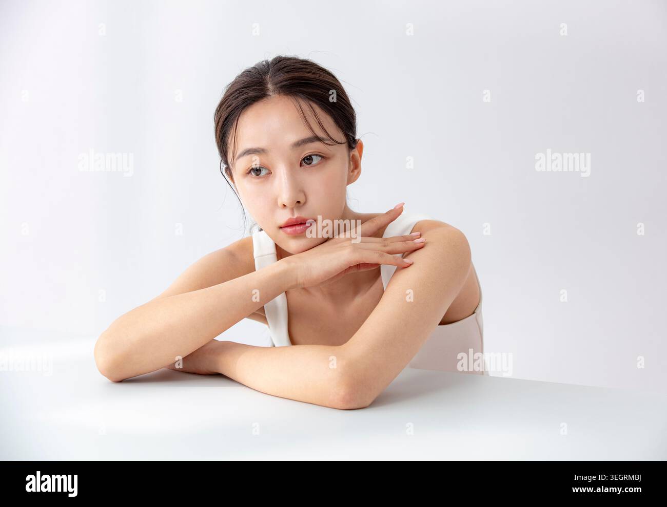 Eine junge Frau sitzt an einem Tisch, den Kopf in den Händen, verloren in Gedanken. Stockfoto